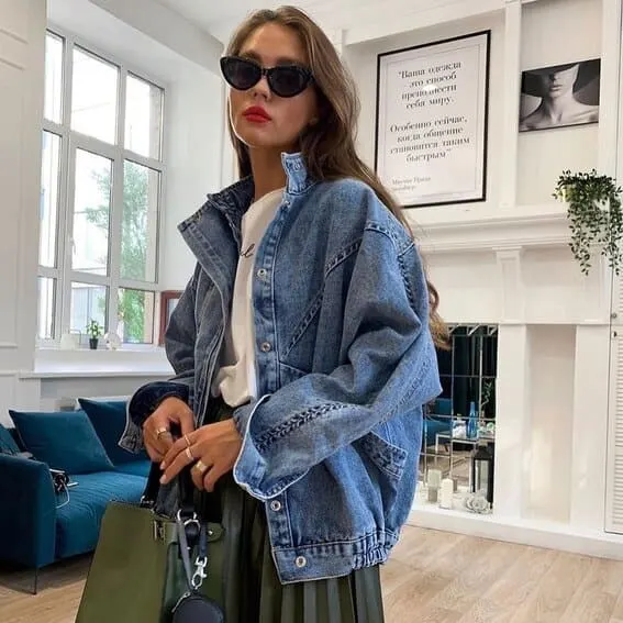 Woman wearing an over-sized denim jacket, glasses and a pleated skirt,