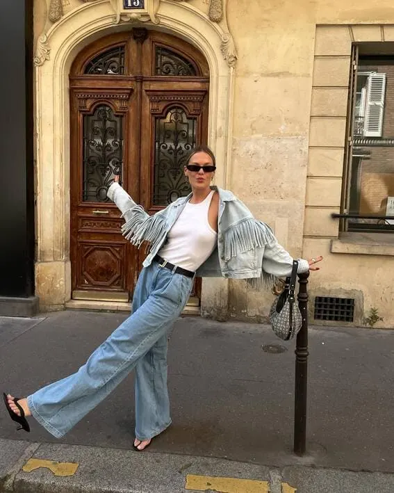 A woman in fringe denim jacket, wide-leg jeans and a white tank top.