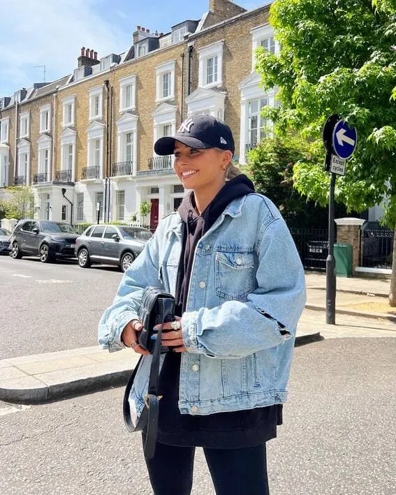 Woman wearing a huge denim jacket with baseball cap and hoodie