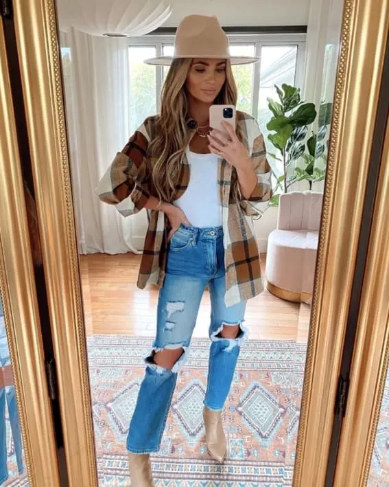 Woman in a trendy fall outfit with a plaid shirt and wide-brim hat.