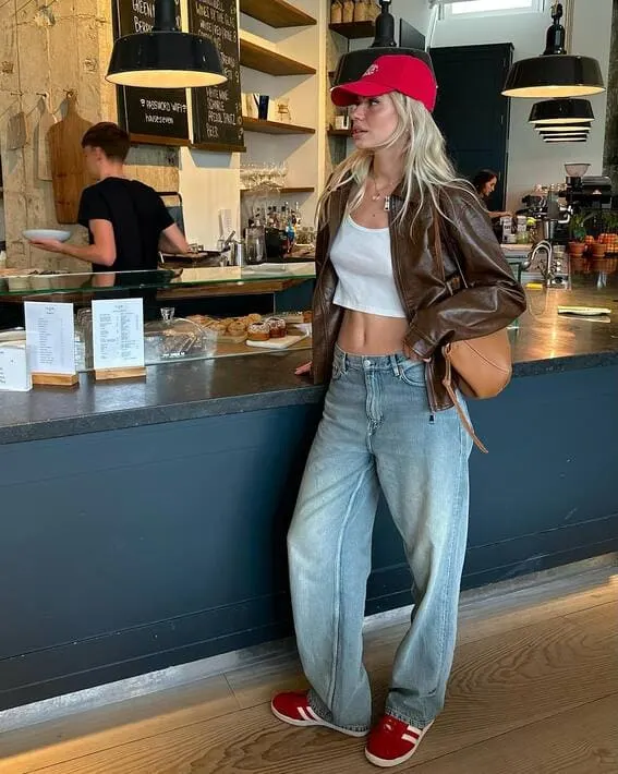 Woman in a casual fall outfit with a leather jacket and red cap.