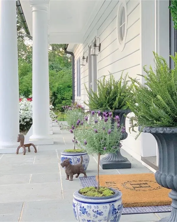 A white-columned porch with blue and white chinoiserie planters, lavender topiaries, ferns, and small decorative animal statues.