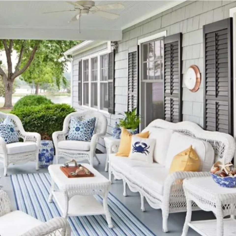 A breezy porch, with light blue floors, white wicker furniture, striped rugs and coastal-themed pillows in navy and yellow.