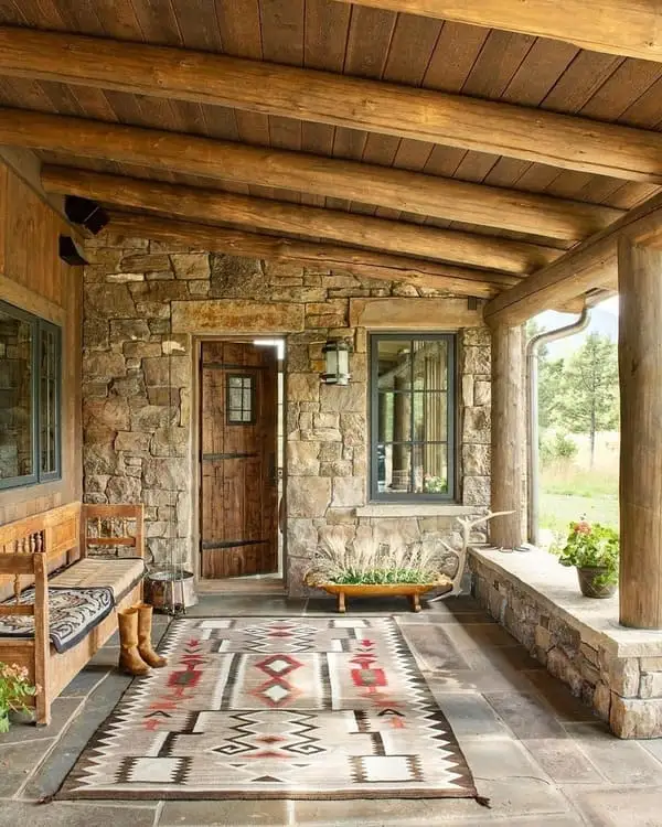 Front porch stone and log, bench made of wood, cowboy boots, tribal-style rug, earthy accents, in a natural setting.