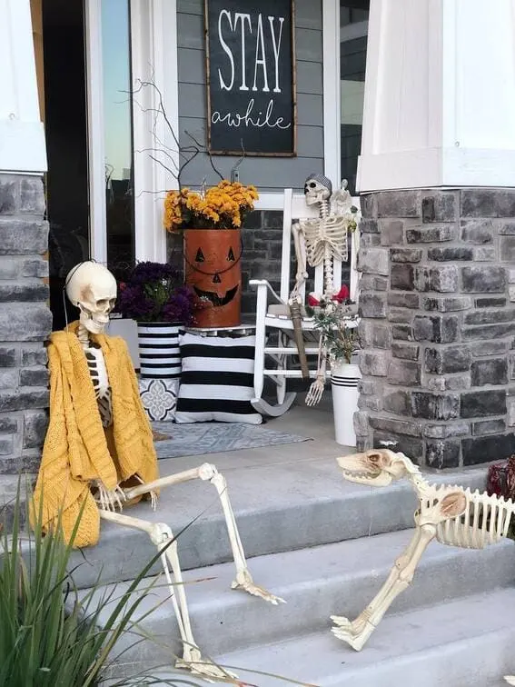 This porch brings a laid-back, playful twist to Halloween with a group of skeletons chilling on the steps, one even wrapped in a cozy mustard-colored sweater!