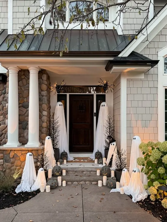 This porch makes a bold Halloween statement with a family of floating ghost figures, draped in flowing white fabric, creating a spooky yet charming vibe.
