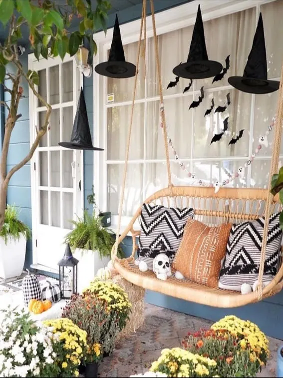 This porch blends cozy comfort with a dash of Halloween magic, featuring floating black witch hats that hang mysteriously above a charming wicker swing.