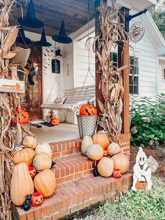 This porch beautifully blends farmhouse coziness with Halloween magic, featuring rustic pumpkins of all shapes and sizes piled on the brick steps.