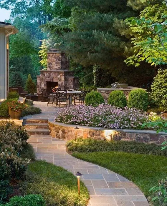 A lush backyard that features an old-fashioned stone fireplace and an attractive garden path.