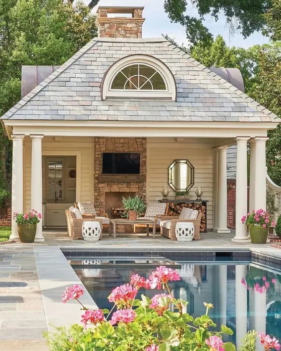 A beautiful poolside patio with an elegant fireplace made of stone and a cozy seating area. Design by @robertdnorris.