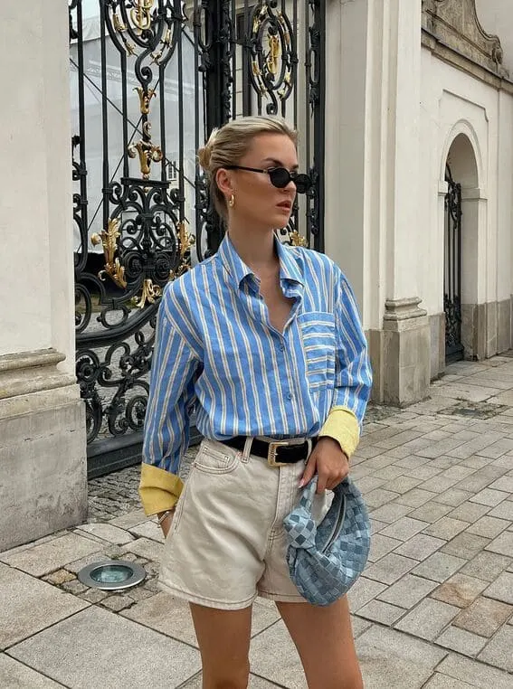A stylish woman wearing a blue and yellow striped oversized shirt paired with beige shorts.