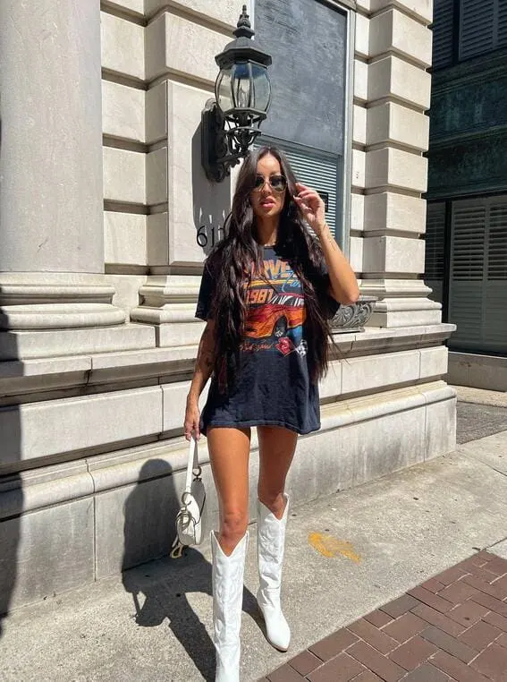 Trendy woman in an oversized graphic T-shirt styled as a dress paired with white cowboy boots.
