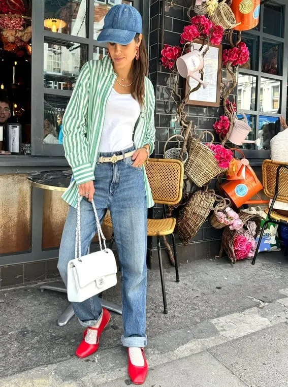 Fashion-forward woman in a green striped oversized shirt paired with jeans, red shoes, and a denim cap.