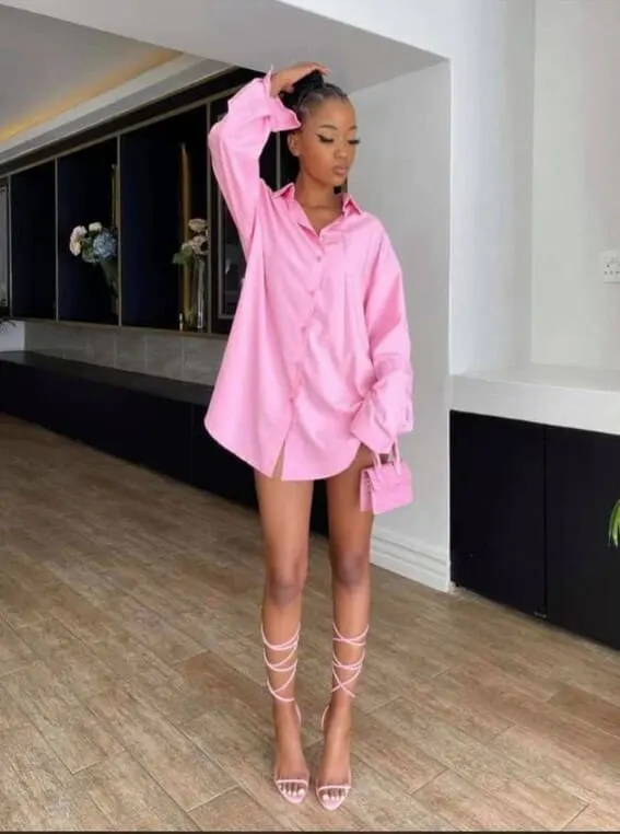 Fashion-forward woman in a pink oversized shirt styled as a dress with matching strappy heels and a mini bag.