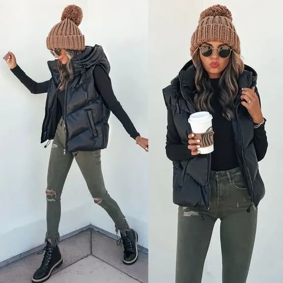 Woman wearing a black puffer vest over a black long-sleeve top, paired with olive green distressed jeans, black boots, a brown chunky knit beanie, and sunglasses. She is holding a coffee cup in one hand.