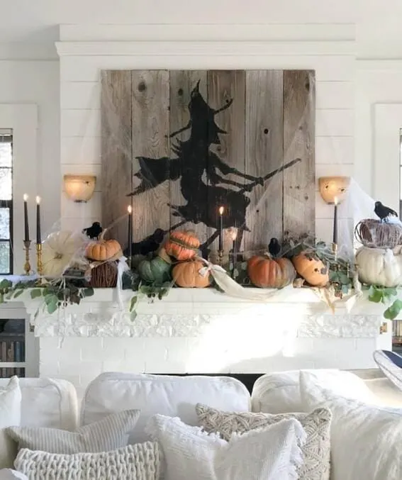 A spooky yet stylish mantel featuring pumpkins, black candles, and a rustic wooden witch silhouette, creating the perfect Halloween atmosphere.