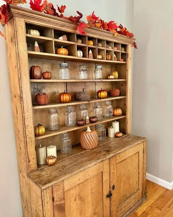 A charming rustic hutch adorned with mini pumpkins, mason jars, and autumn garlands for a cozy fall touch.