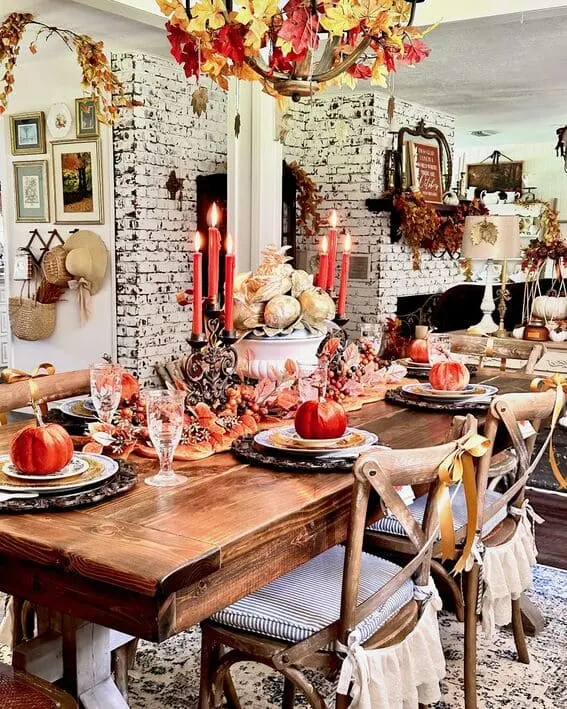 A vibrant fall tablescape featuring velvet pumpkins as place settings, surrounded by rich autumn foliage and glowing candles.
