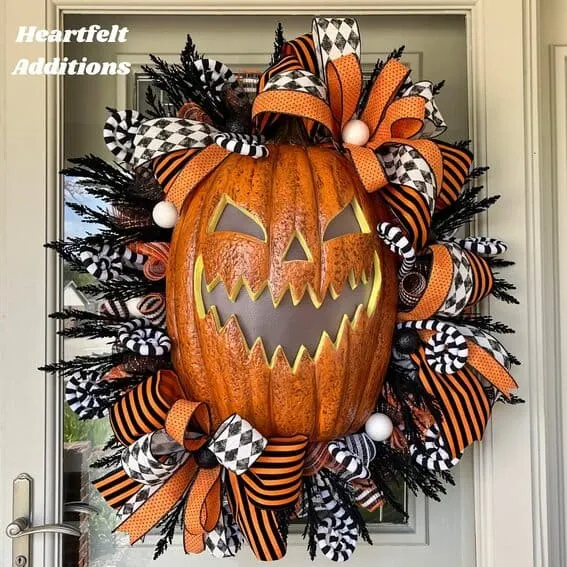 A spooky Halloween wreath featuring a large jack-o'-lantern surrounded by black, orange, and checkered ribbons for a playful yet eerie display.