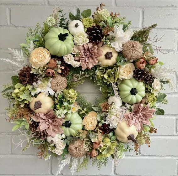 A lush autumn wreath featuring soft green and white pumpkins accented with pinecones, dahlias, and creamy florals.