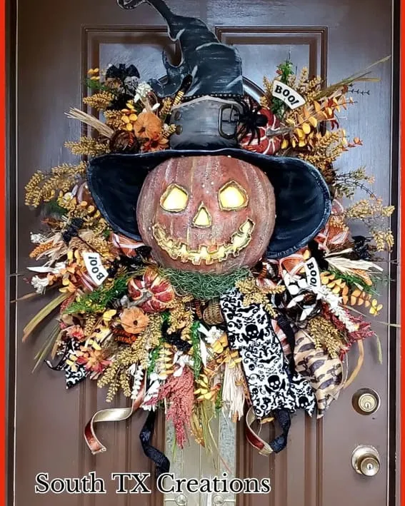 A bold and playful Halloween wreath featuring a glowing jack-o'-lantern with a witch's hat, surrounded by autumn florals and spooky accents.