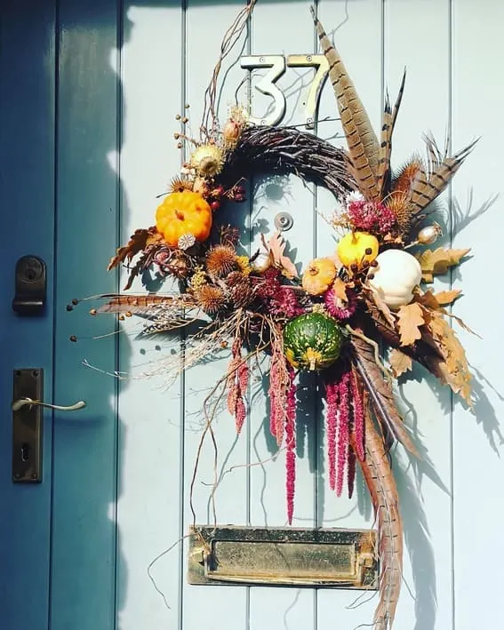 A beautifully crafted rustic wreath featuring vibrant gourds, feathers, and natural autumn elements for a woodland-inspired fall look.