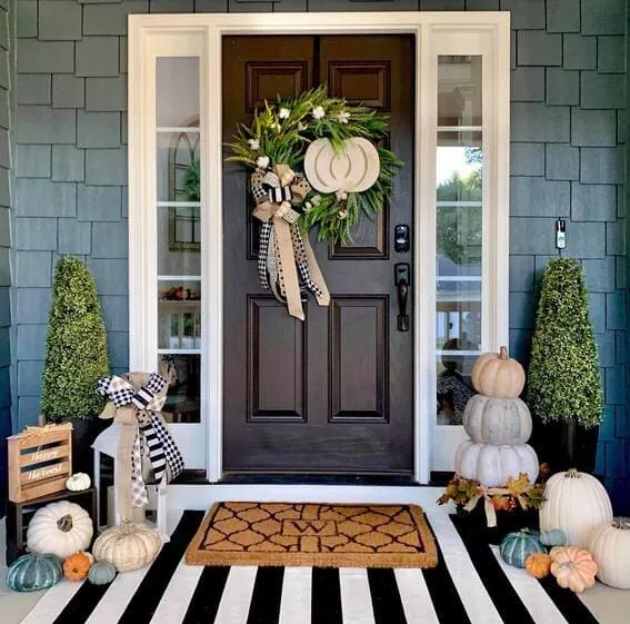 A stylish wreath featuring a blend of fresh greenery, white pumpkins, and a gingham ribbon for a modern farmhouse touch.