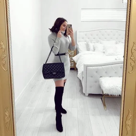 A woman is wearing an oversized turtleneck sweater with over-the-knee-boots.