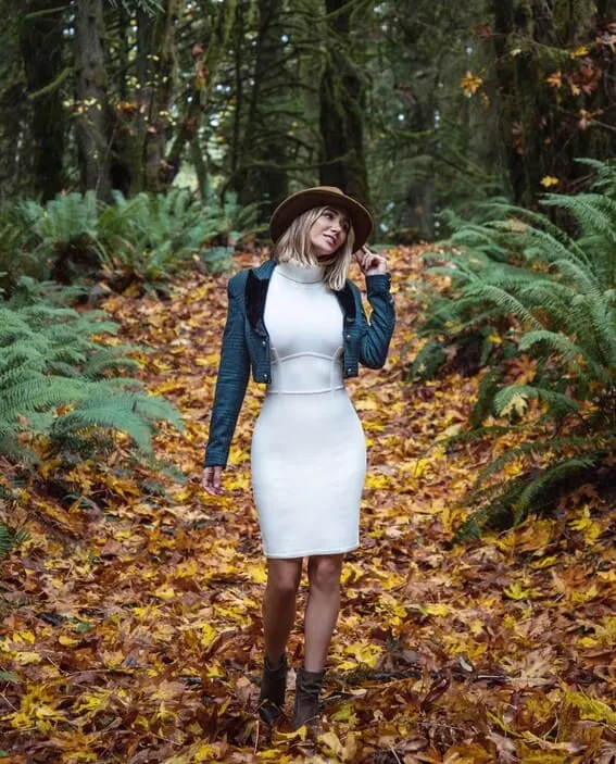 A woman in a white turtleneck sweater with an uncut jacket and large-brim hat.
